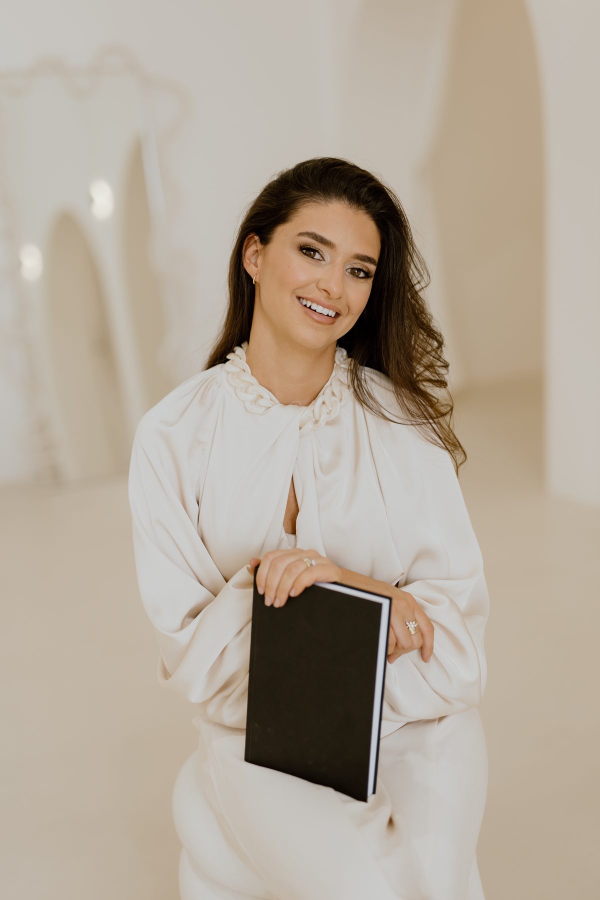 Camila, smiling, holding a notebook in a softly lit studio