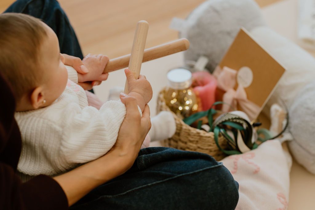 An adult's hands gently guiding a baby's grip on a wooden percussion stick