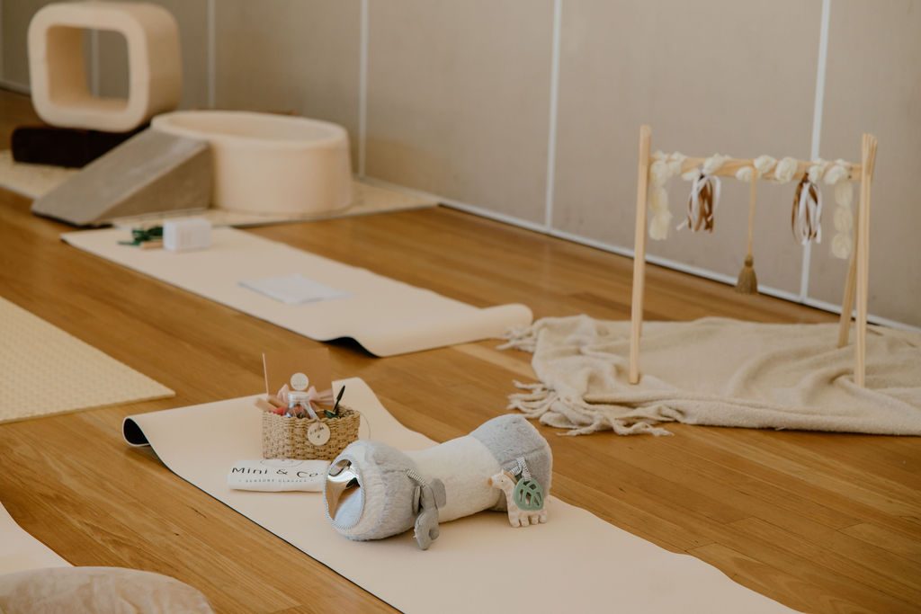 A softly lit sensory-play space with cream mats, a Mini & Co. branded mat, a woven basket and foam play shapes