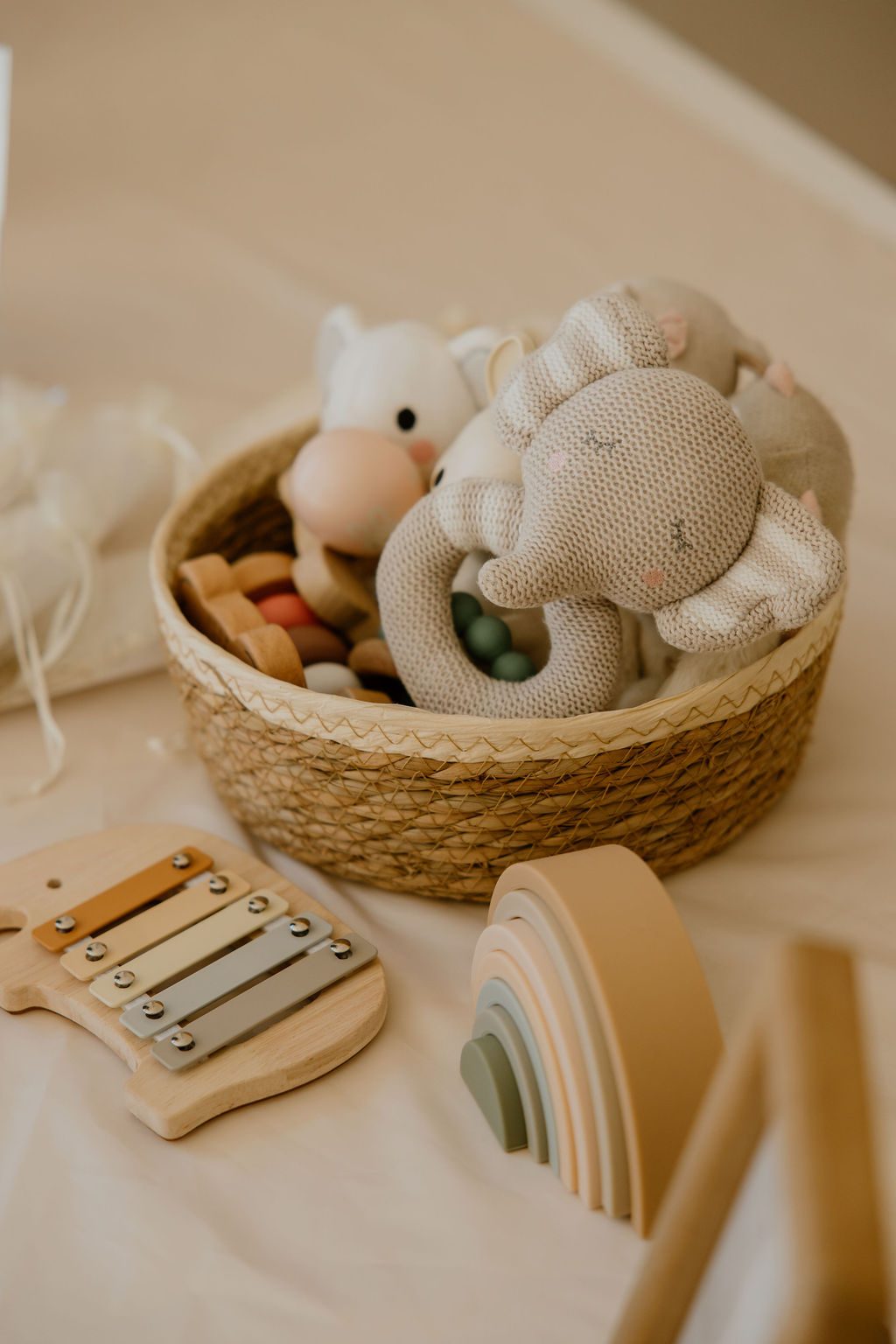 A woven basket of knitted soft toys beside a wooden xylophone and pastel stacking rainbow