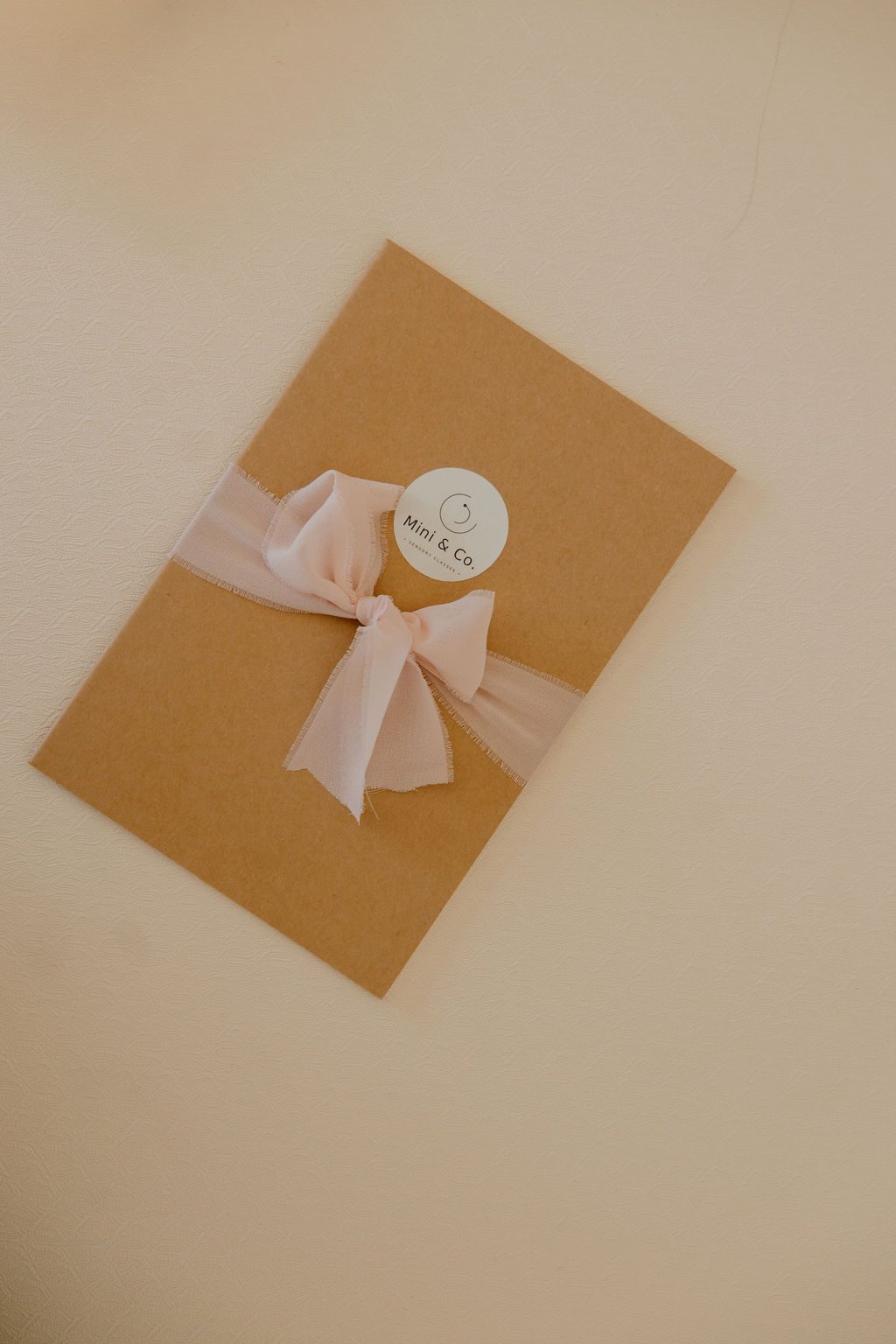 A kraft-paper welcome gift tied with a blush silk ribbon and a round Mini & Co. logo sticker
